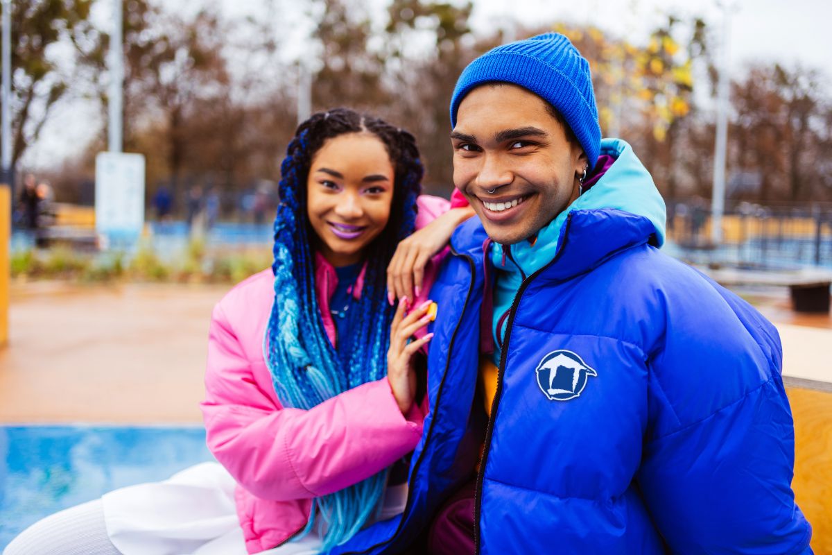 A couple wearing vibrant jackets smiles and poses together for a photo outdoors.