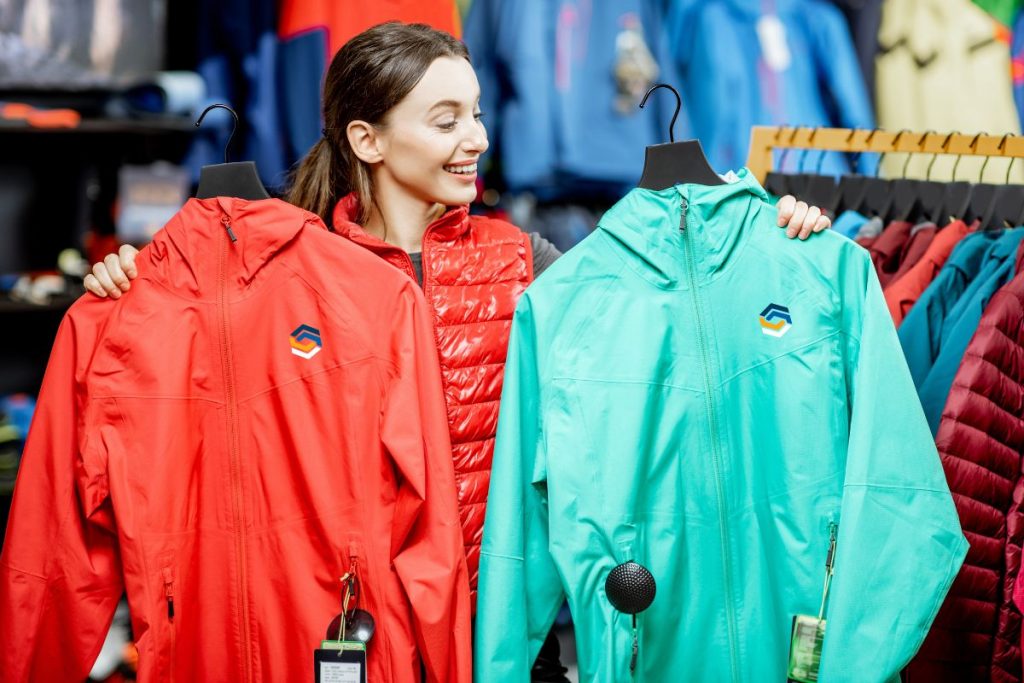 A woman holds two jackets while shopping in a clothing store.