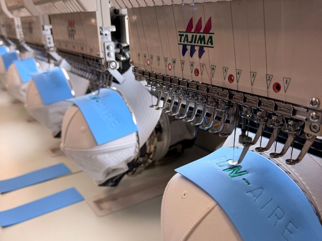 A close-up view of custom hats being embroidered with the "BON-AIRE" logo, showcasing the precision and quality of the embroidery process at White House Custom Apparel & Graphics in St. Petersburg.